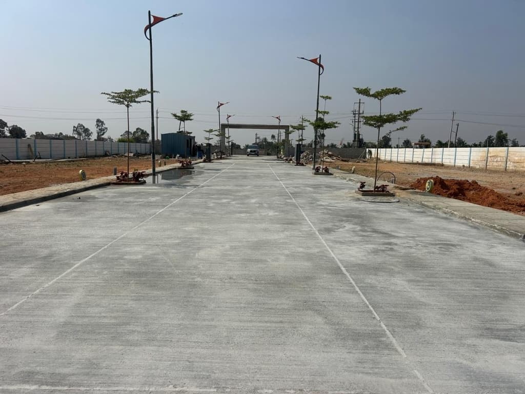 Chamundeshwari Residency wide paved road leading towards layout entrance archway